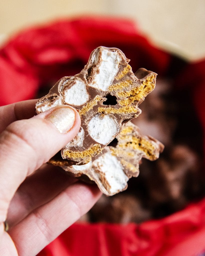 A hand holding a cut open marshmallow golden graham chocolate candy cluster.