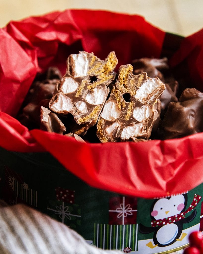 A close up of a s'mores cluster cut in half showing mini marshmallows, and golden graham cereal surrounded in chocolate.