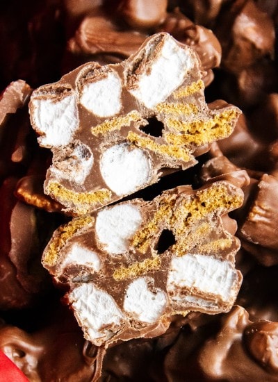 A close up of a s'mores cluster cut in half showing mini marshmallows, and golden graham cereal surrounded in chocolate.