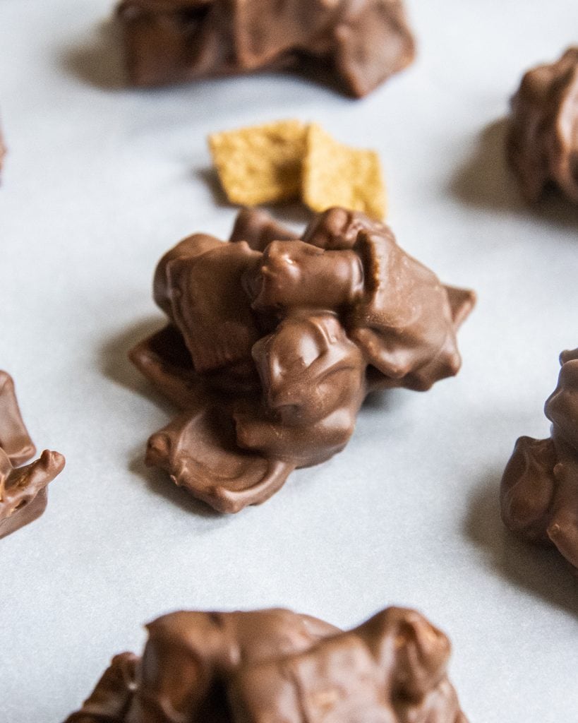 A s'mores cluster on parchment paper, with the edges of more clusters on the edges of the photo.