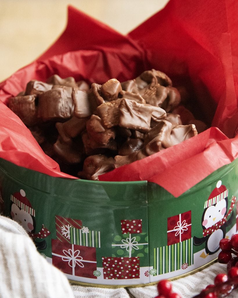 A metal holiday tin filled with red tissue paper and chocolate s'mores clusters.