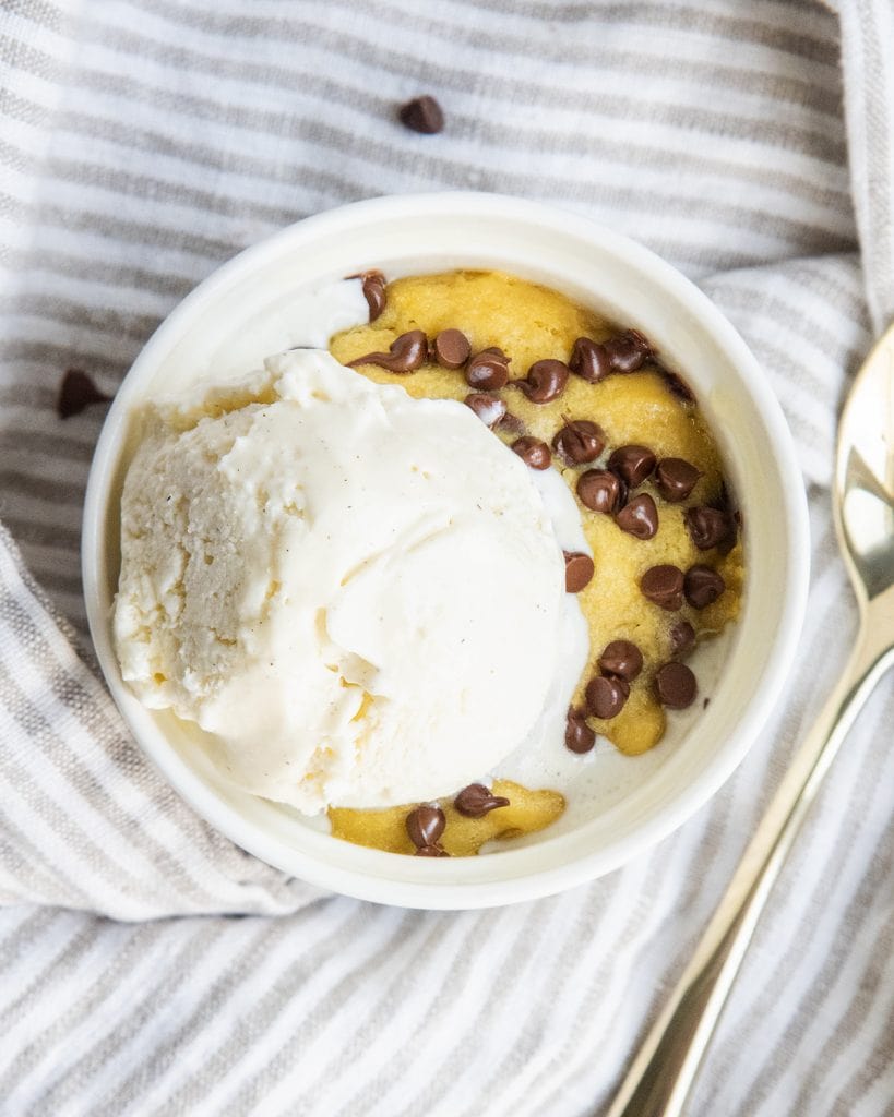 An overhead photo of a chocolate chip cookie in a mug with a scoop of ice cream on top.