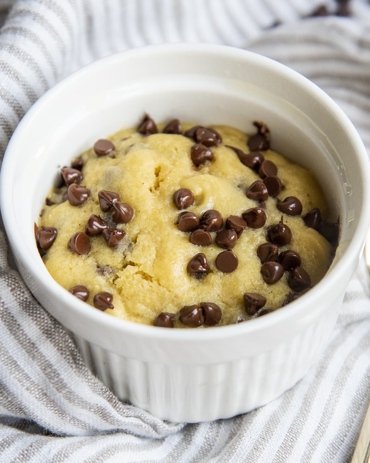 Chocolate chip cookie in a white ramekin, made in the microwave, and topped all over with mini chocolate chips.