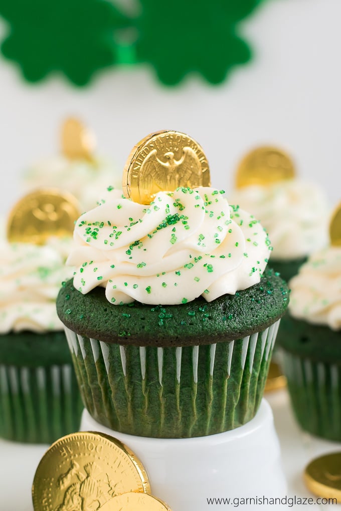 A green cupcake topped with white cream cheese frosting and a chocolate gold coin.