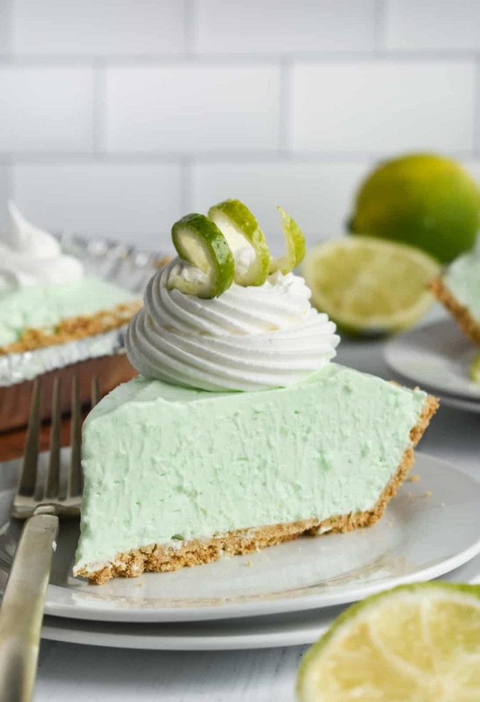 A slice of lime jello pie on a plate, topped with whipped cream, and a lime peel swirl.