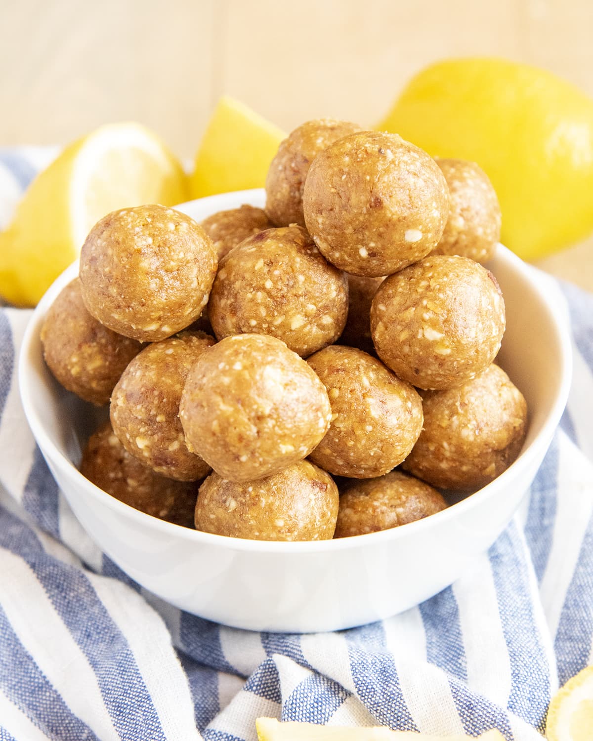 A white bowl full of lemon energy balls on a blue and white striped cloth.