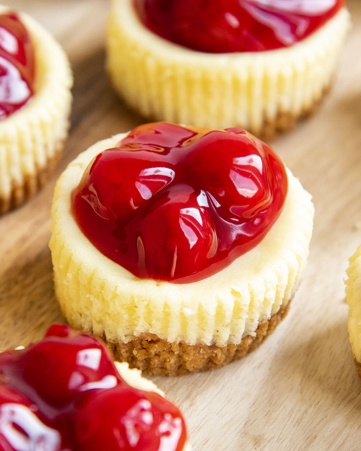 A close up of mini cherry cheesecakes, with ridges from a muffin paper liner on the sides, and 4 canned cherries on top.