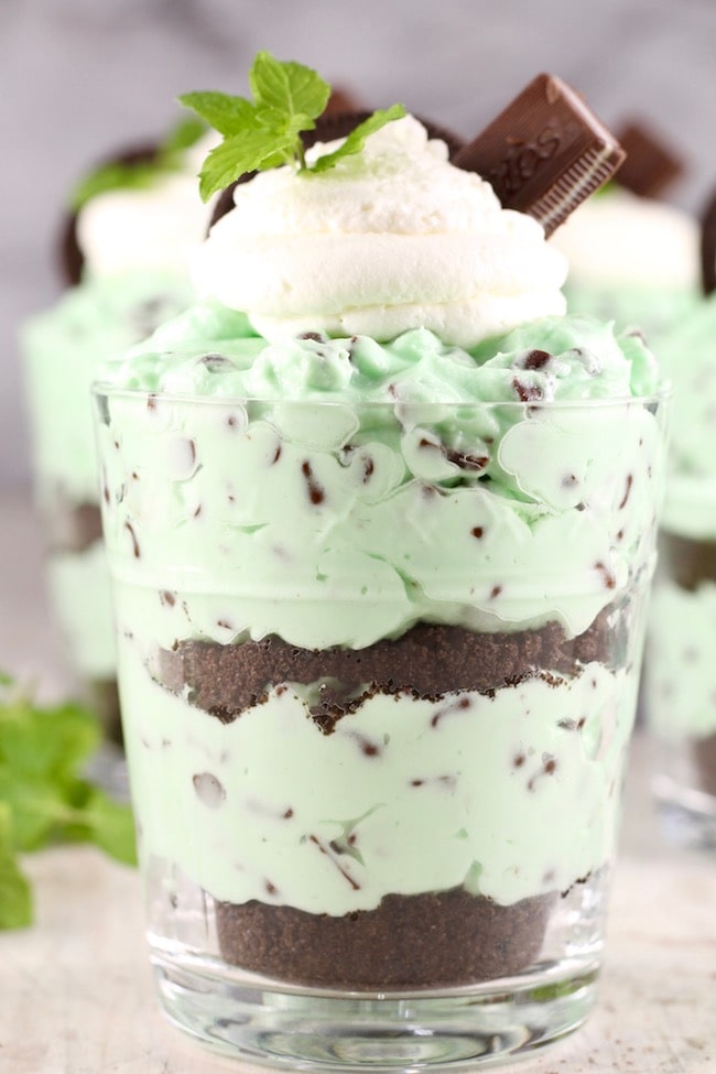 A no bake mint chocolate chip cheesecake in a cup with layers of Oreo crust.