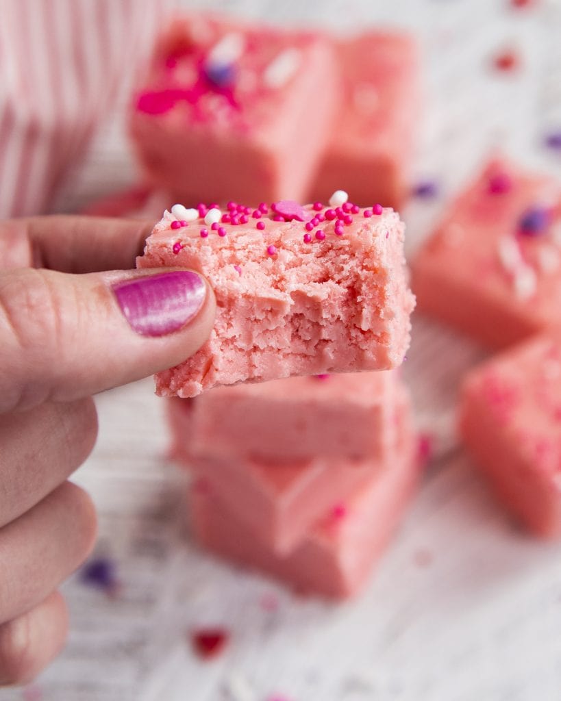 A hand holding a piece of pink fudge with a bite out of it.