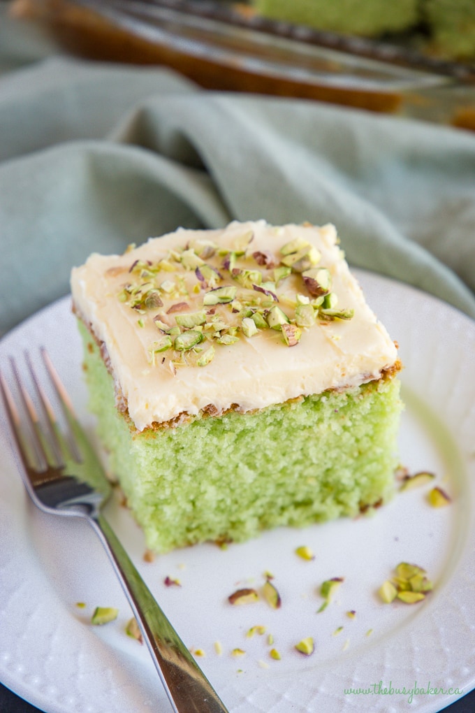 A piece of pistachio pudding cake with a cream cheese frosting on top, on a plate.