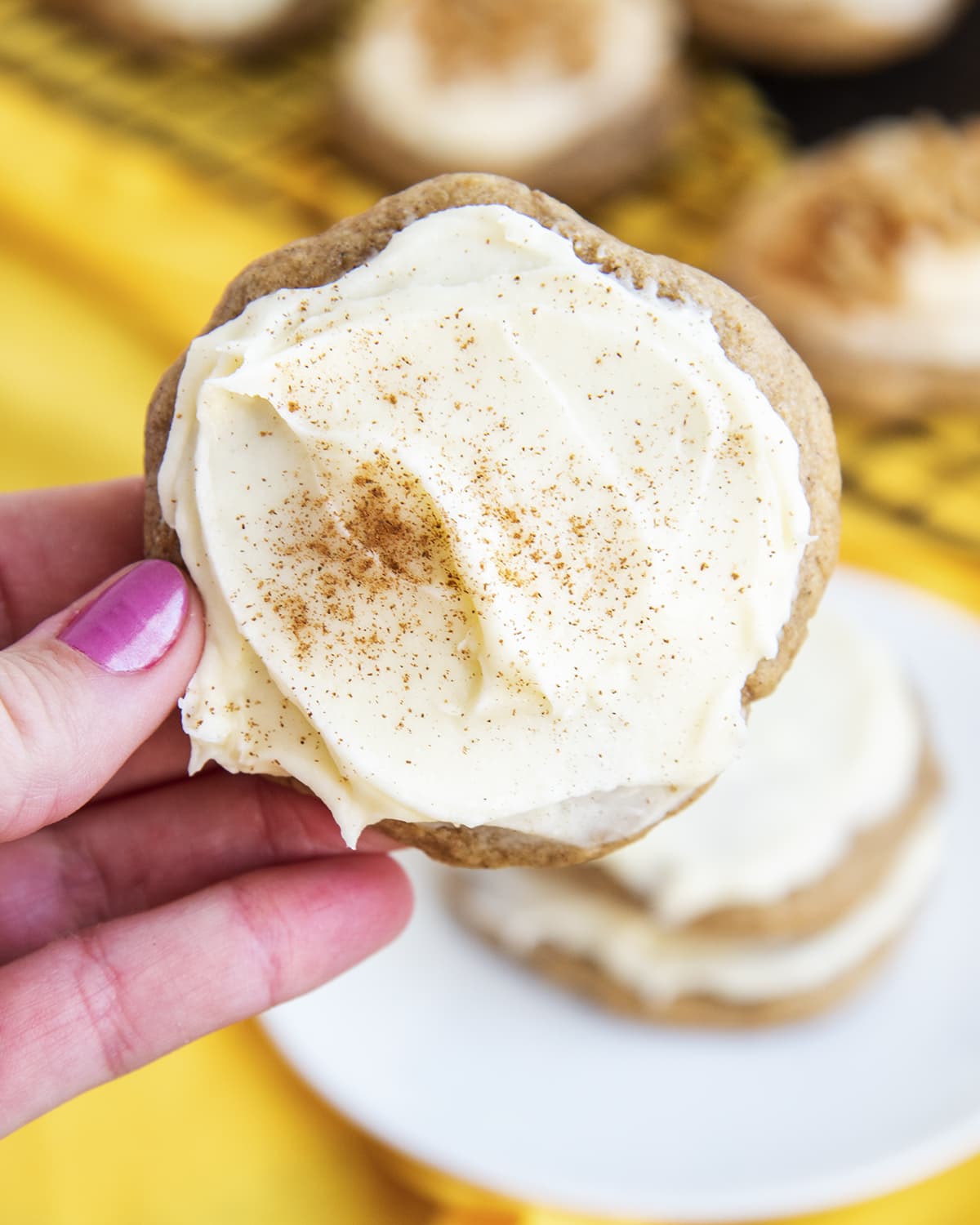 A hand holding a cream cheese frosted banana bread cookie.