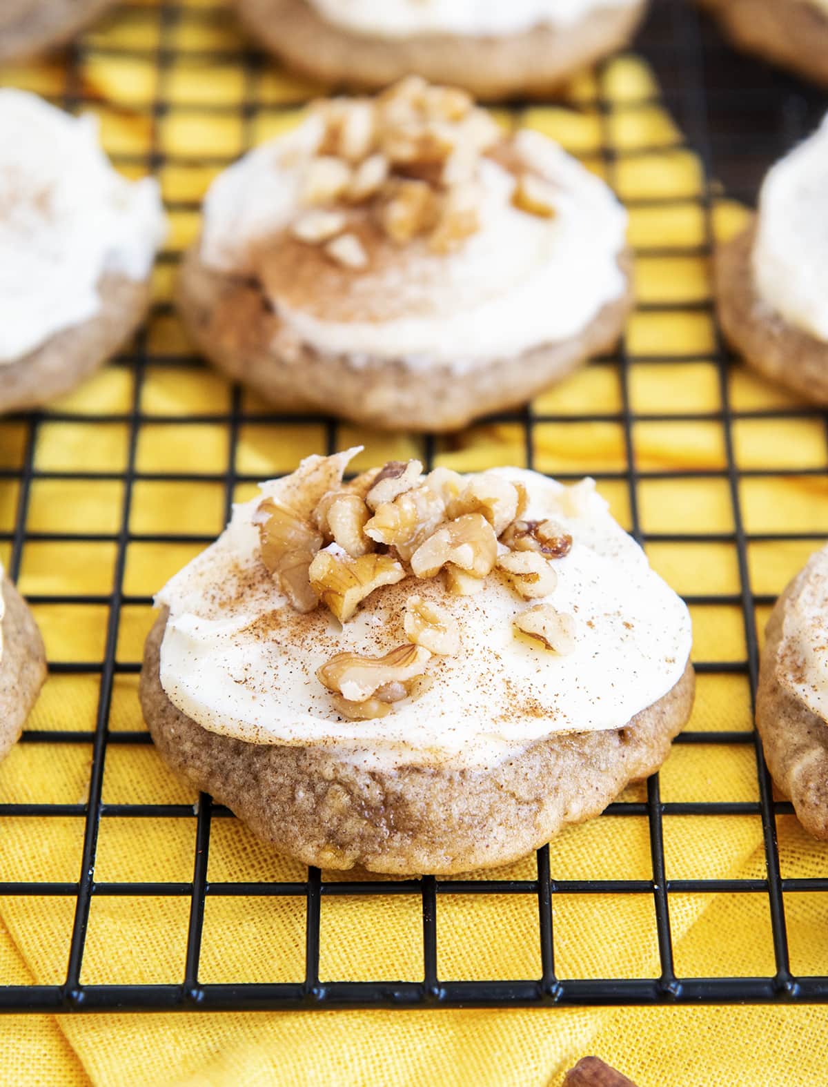 Banana bread cookies on a cooling rack topped with cream cheese frosting and chopped walnuts.