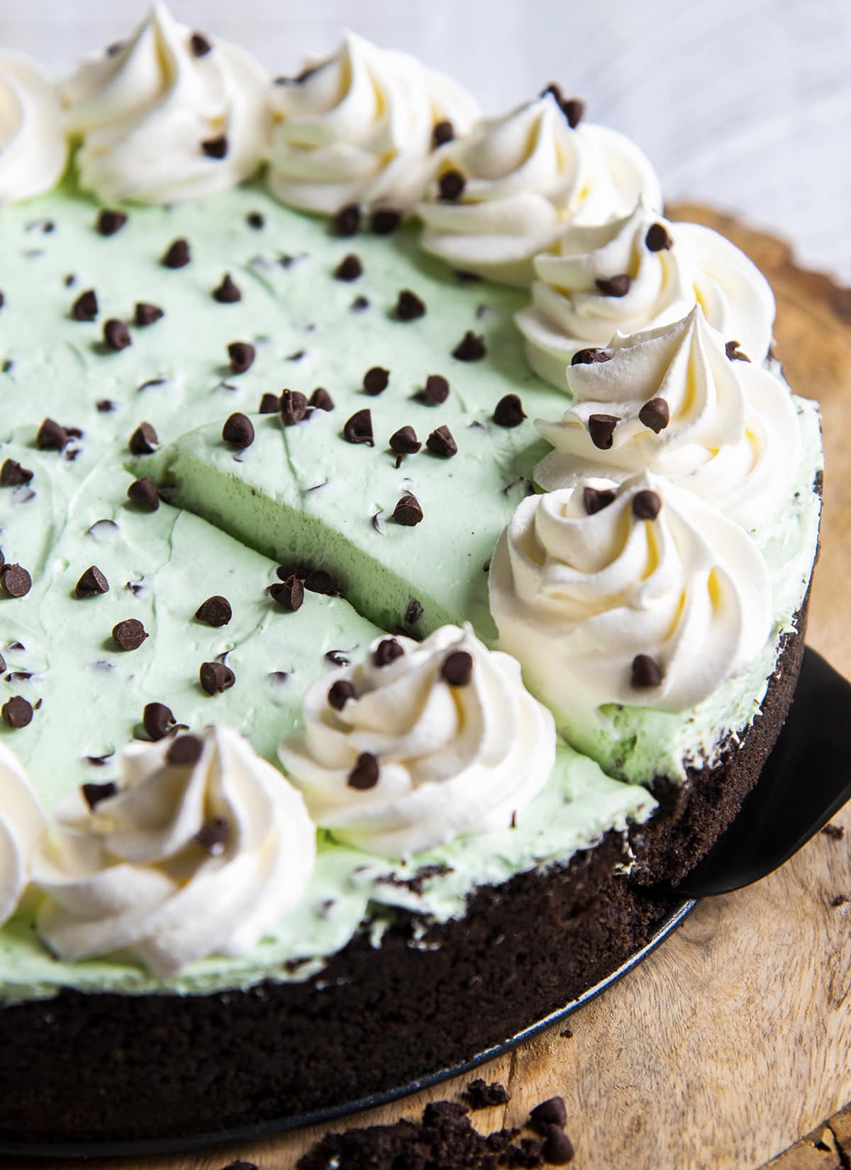 A slice of mint chocolate cheesecake being lifted out of the cheesecake on a pie server.