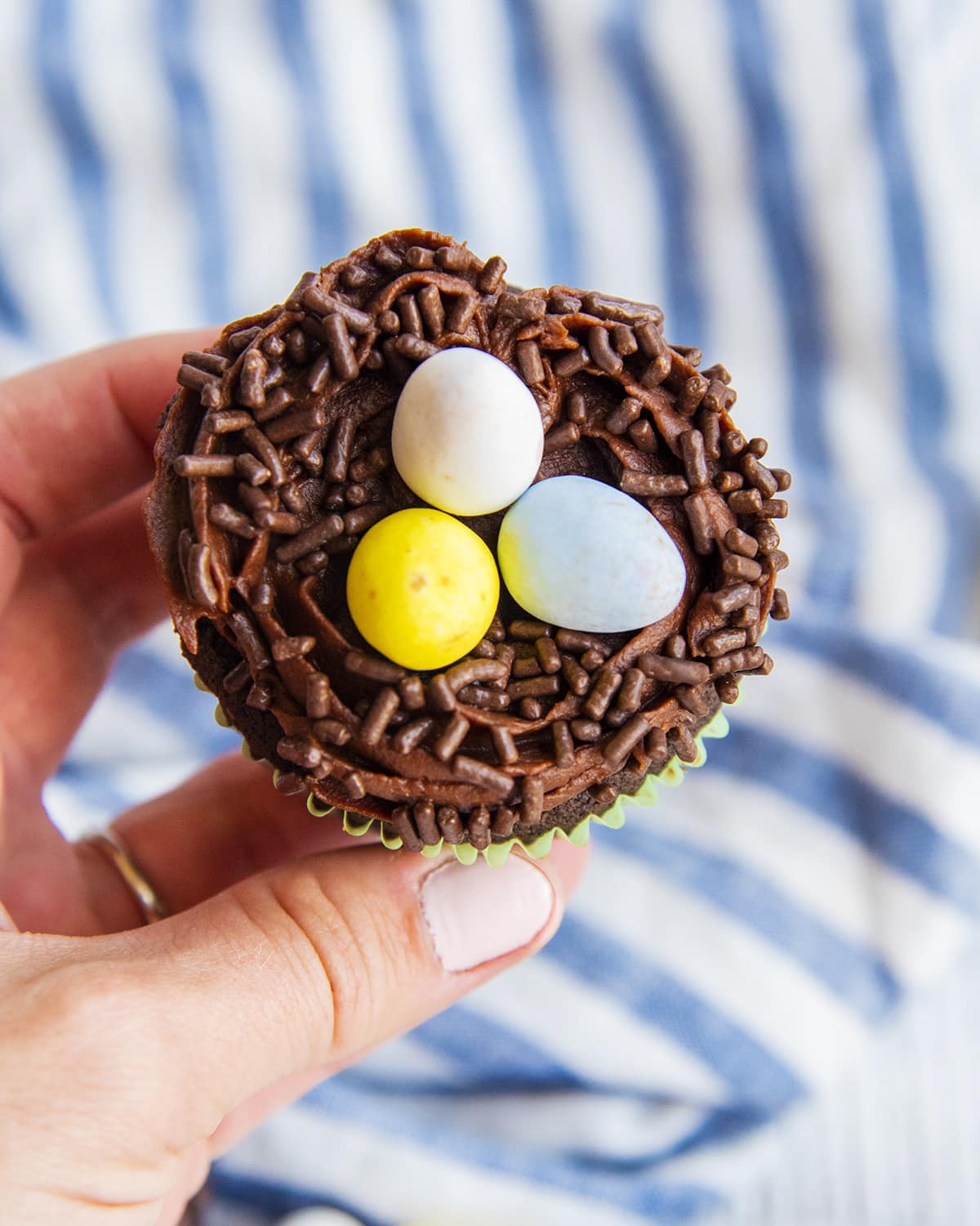 A hand holding a bird's nest cupcake.