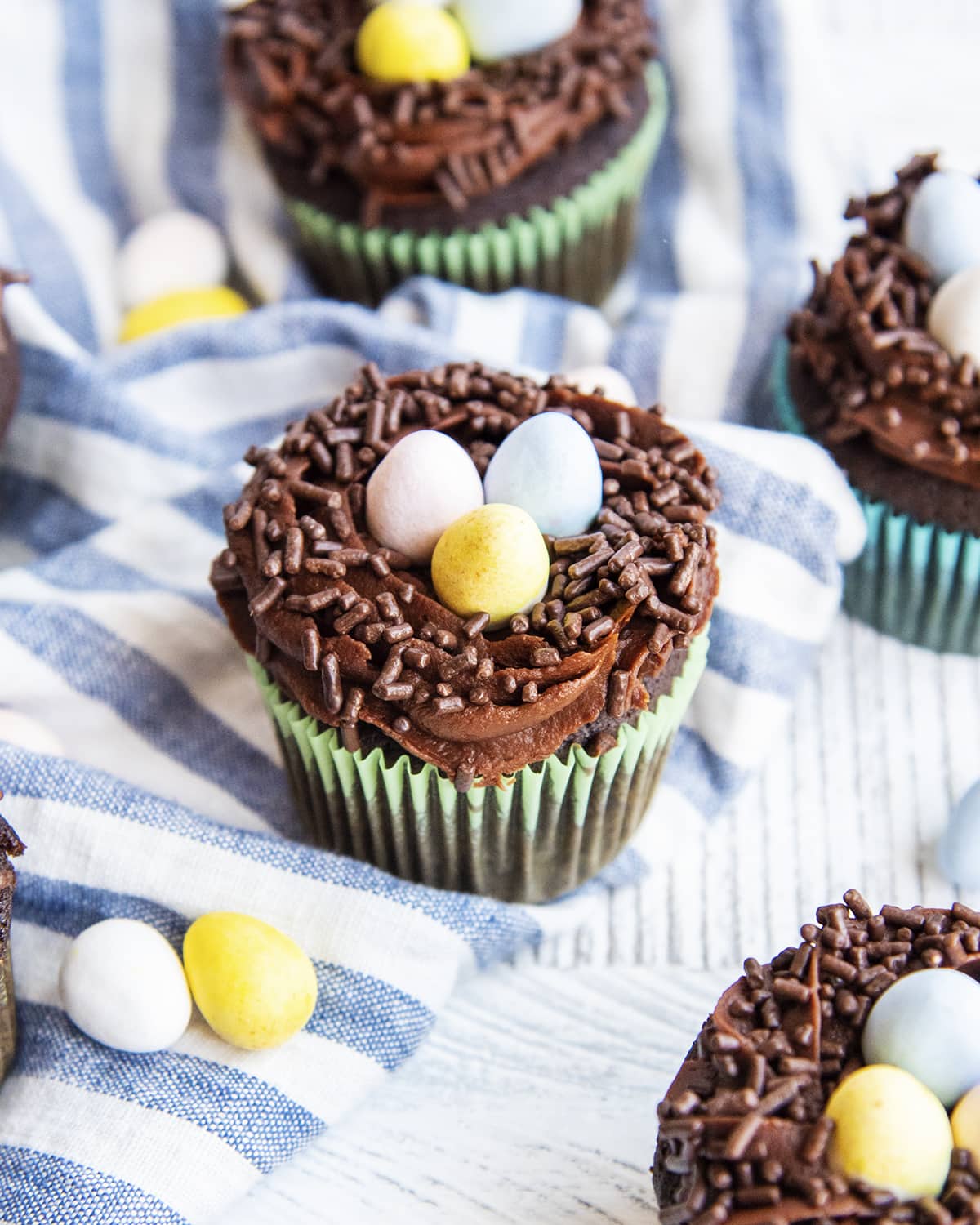 Chocolate bird's nest cupcakes on a blue and white cloth.