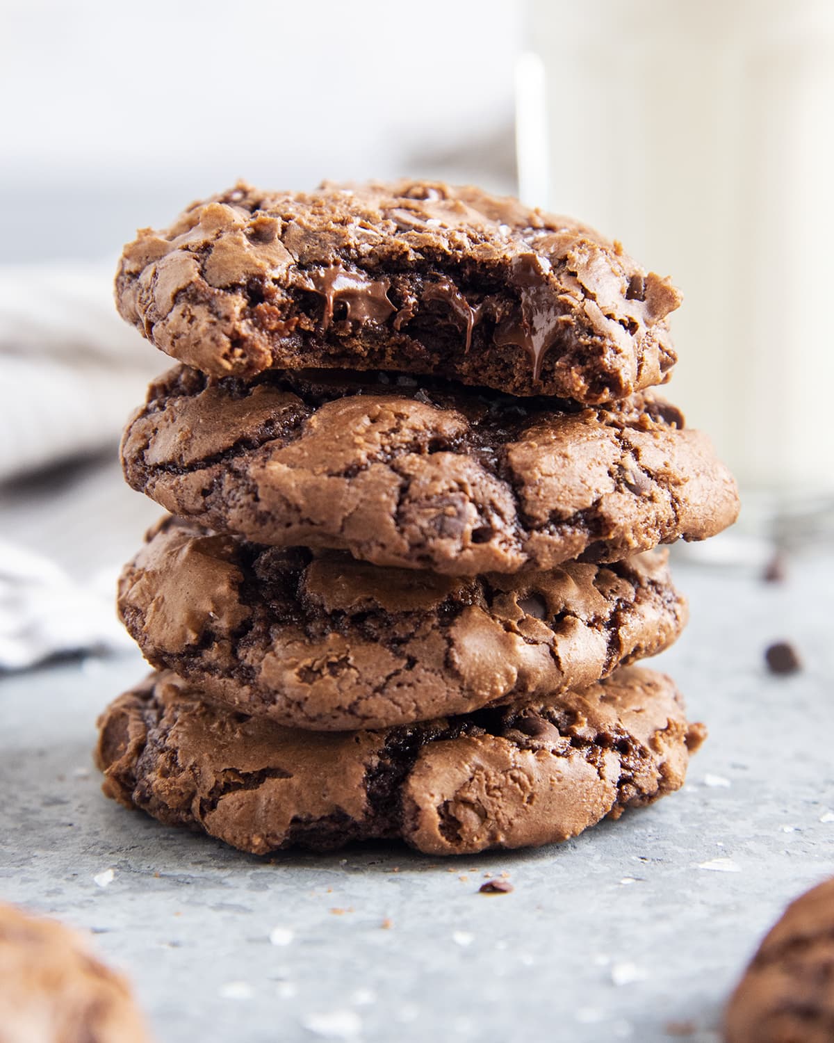 Four brownie cookies in a stack, the top cookie has a bite out of it and is showing melted chocolate chips in the middle.