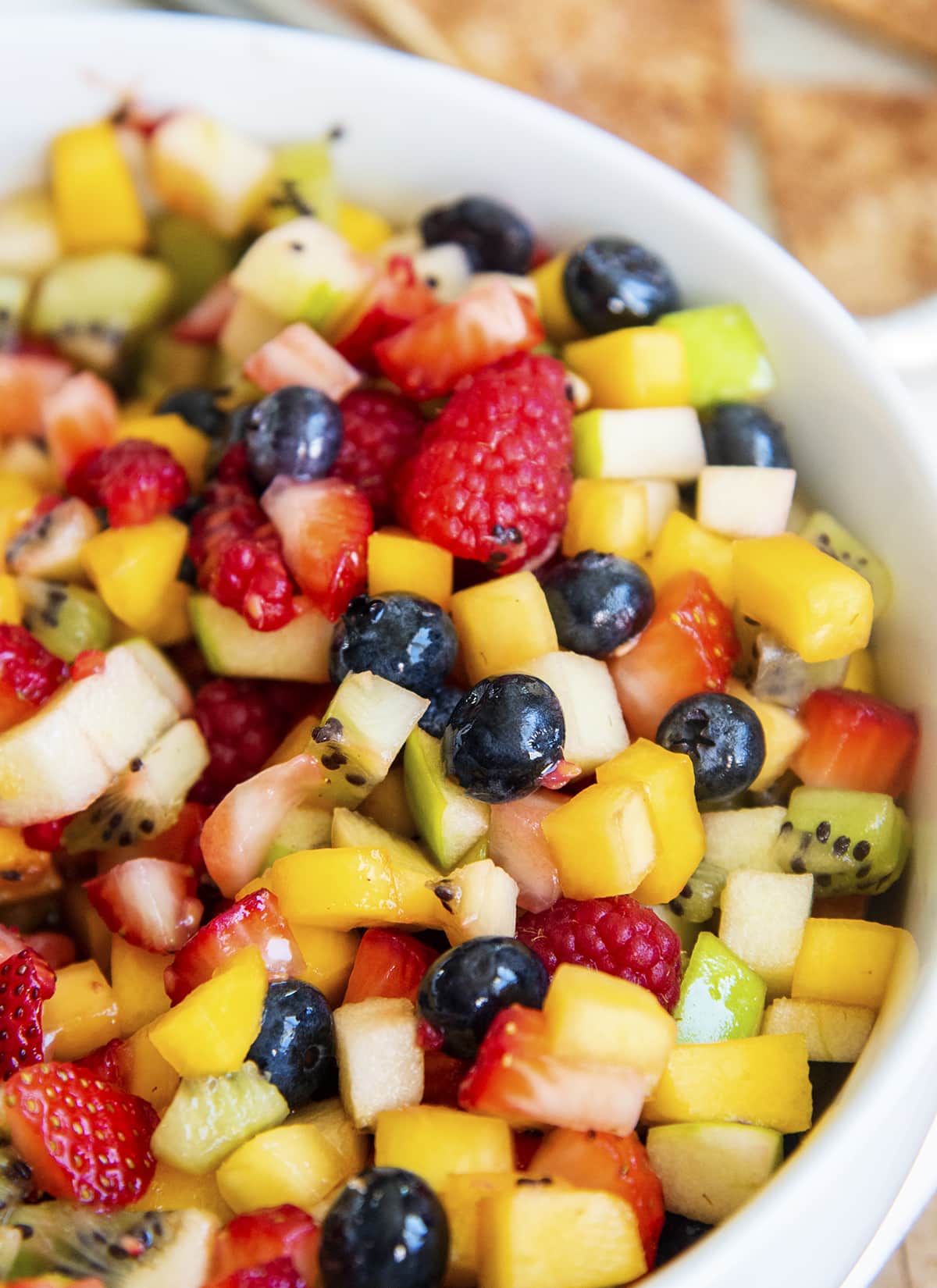 A close up of a bowl of fruit salsa with strawberries, blueberries, raspberries, kiwi, mango, and apple pieces.