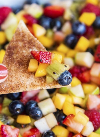 A hand holding a cinnamon tortilla chip with fruit salsa on it.