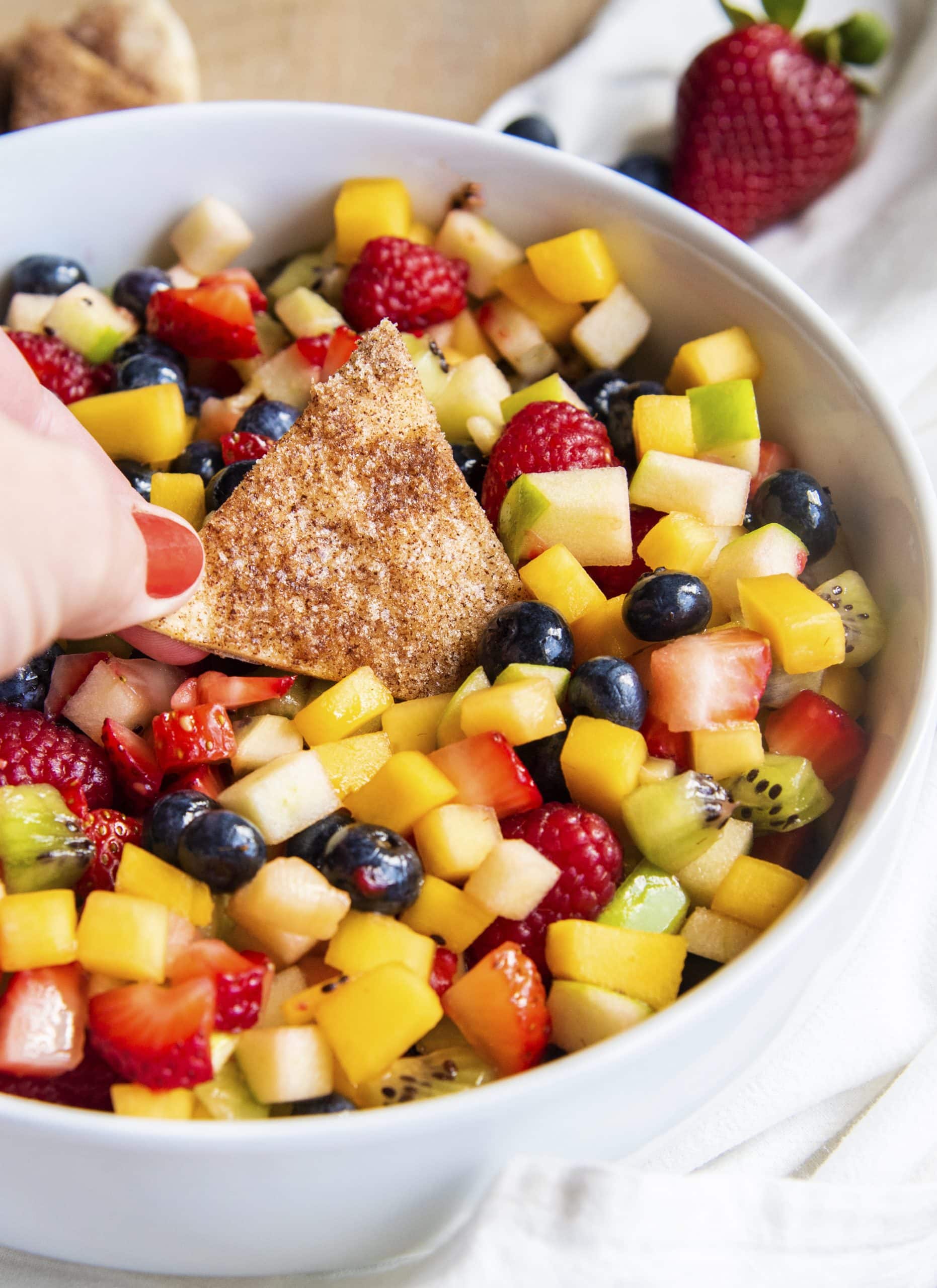 A cinnamon chip dipping into a bowl of fruit salsa.