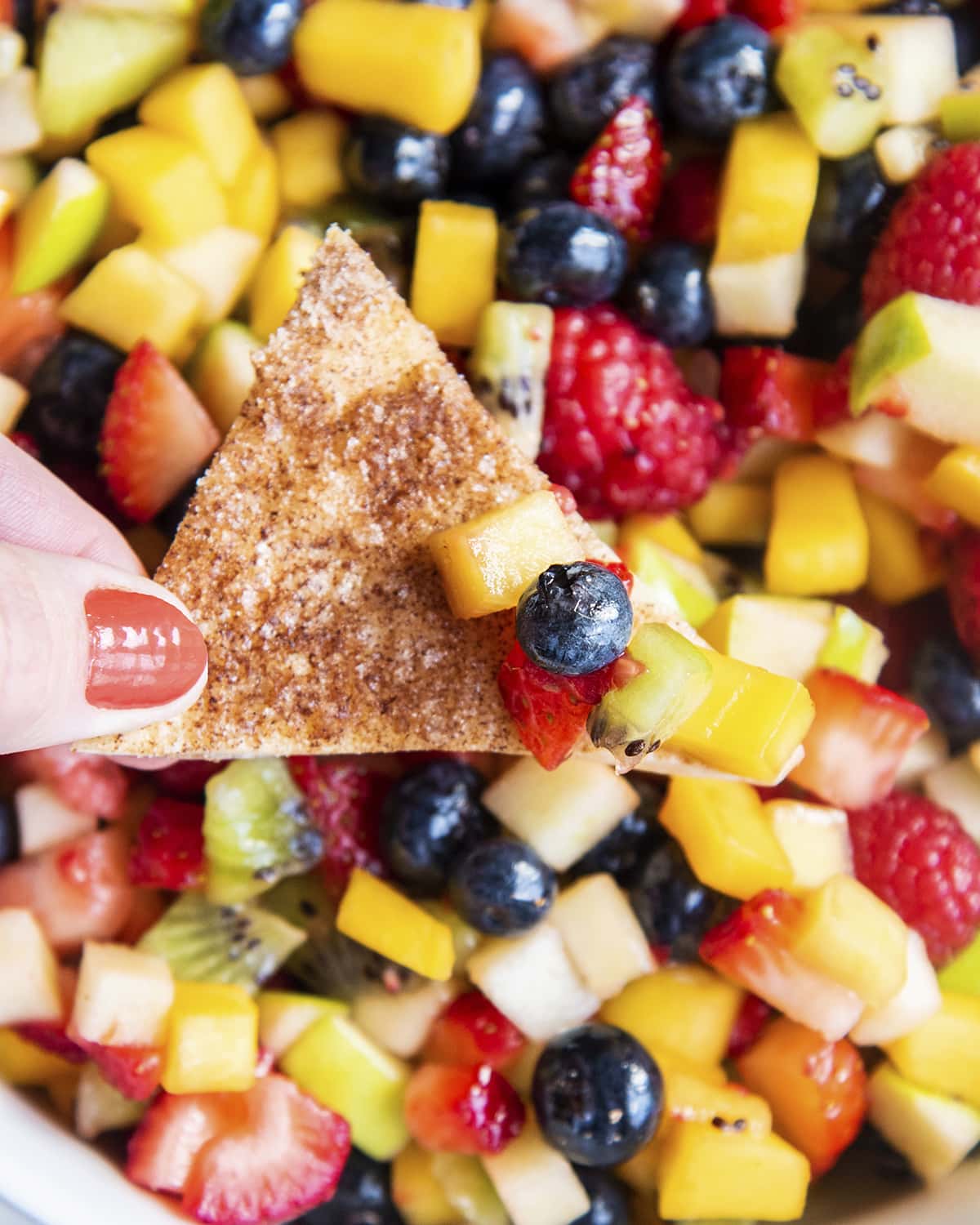 A cinnamon tortilla chip dipping into a bowl of fruit salsa.