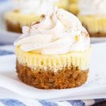 A close up of a mini carrot cake cheesecake cupcake, topped with whipped cream.