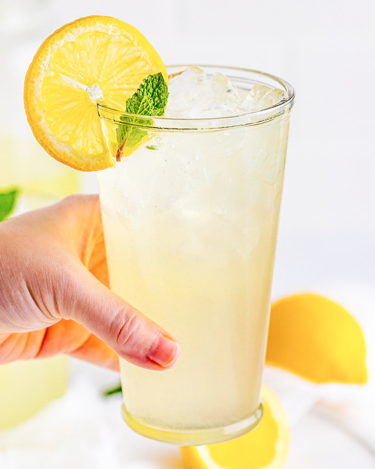 A hand holding a glass of iced lemonade.