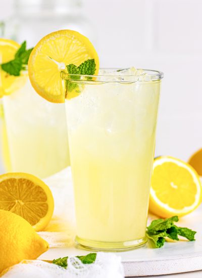 A cup of lemonade with a lemon slice and mint on top.