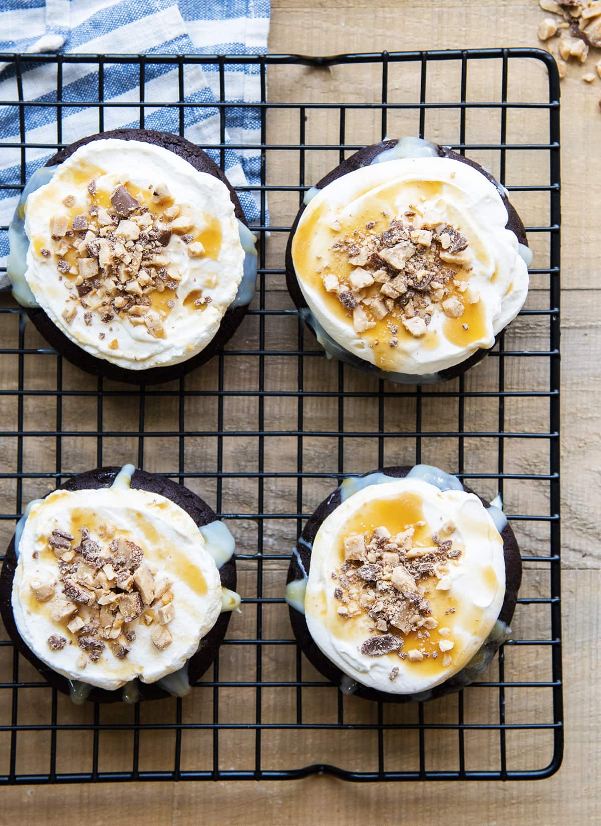 Chocolate cookies topped with whipped cream, and heath toffee pieces on a cooling rack.