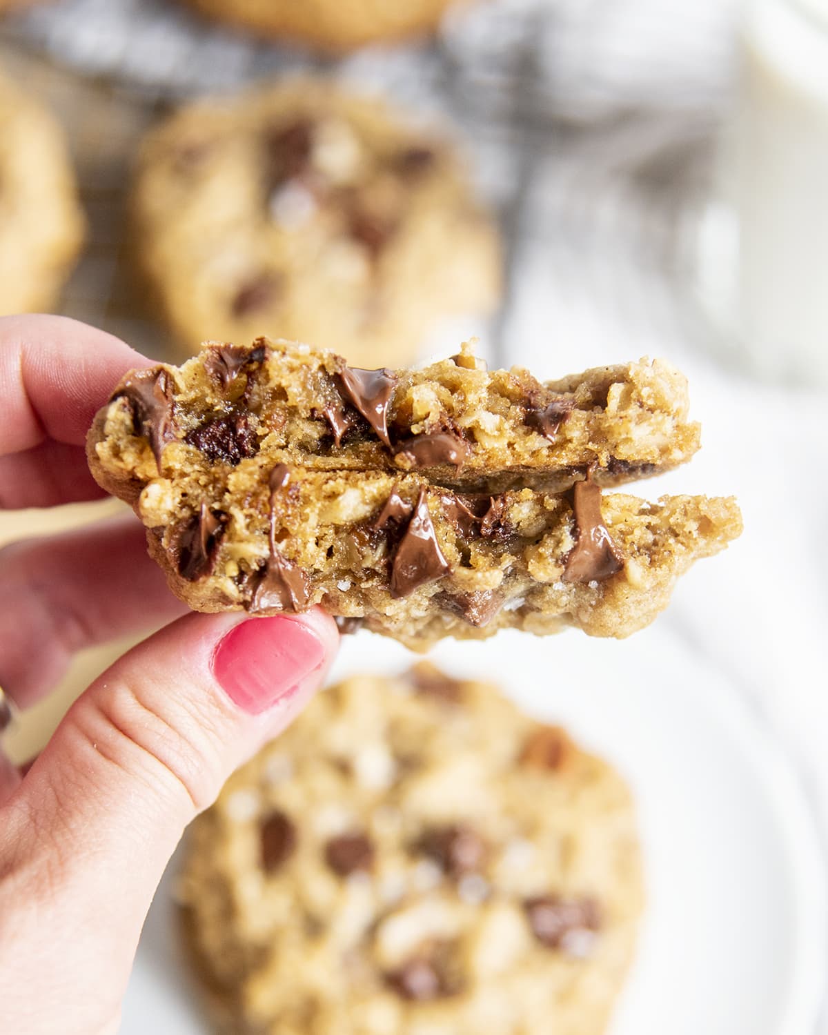 A hand holding two halves of a cowboy cookie showing the oatmeal cookie, and chocolate chips in the middle.