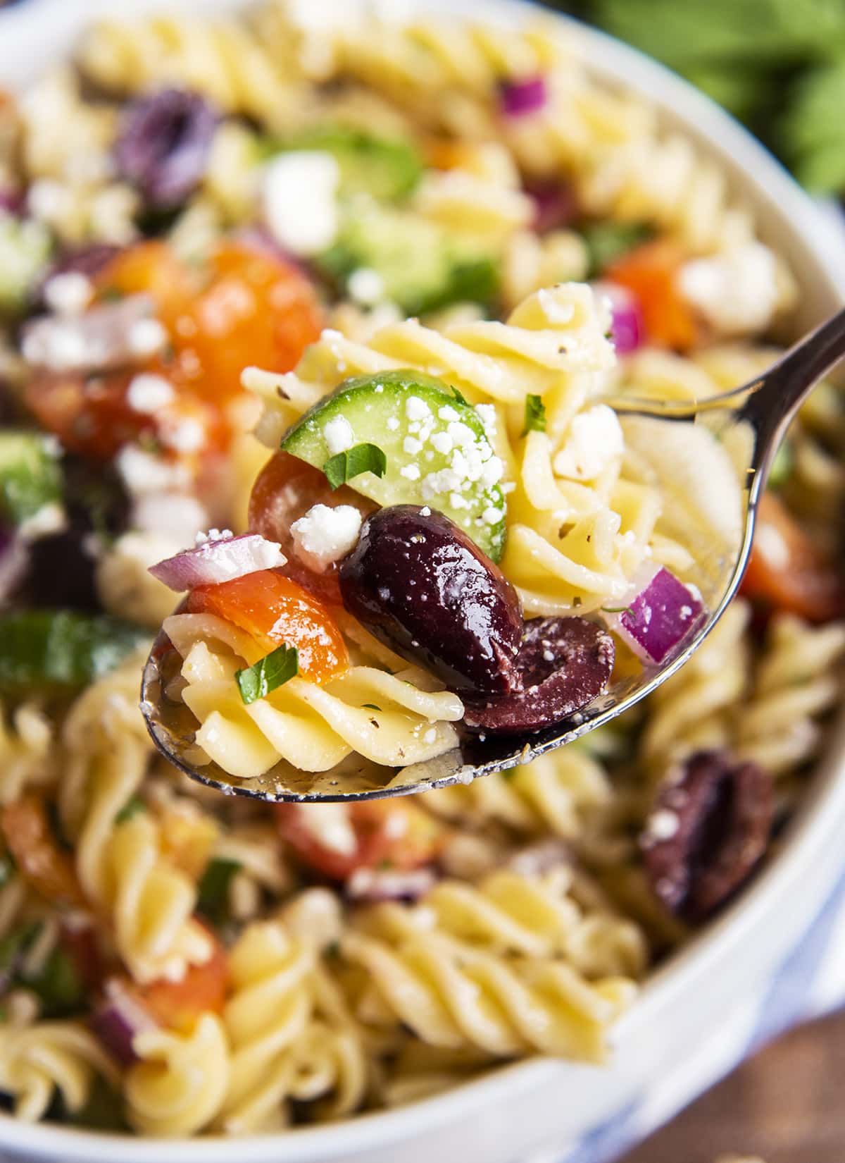 A spoonful of greek pasta salad with rotini, kalamata olives, tomatoes, and cucumbers.