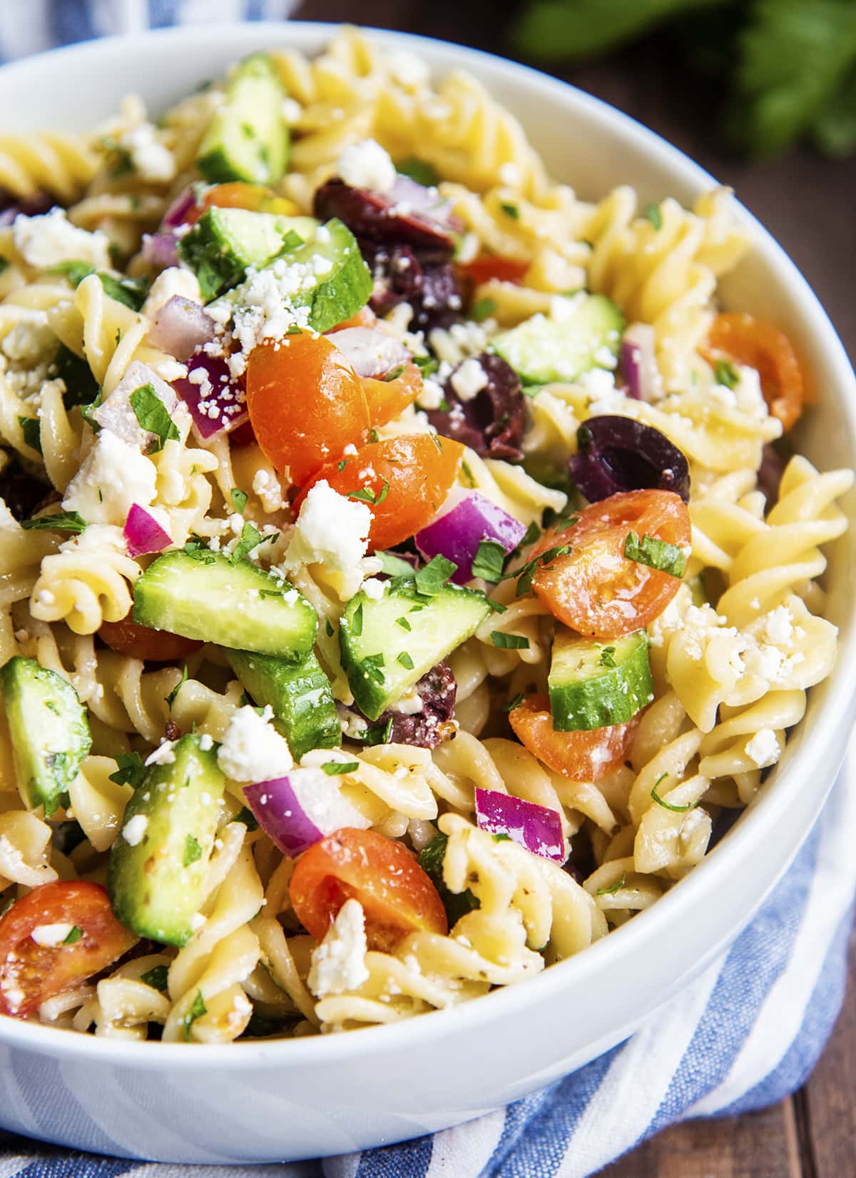 A bowl of greek pasta salad topped with feta cheese crumbles.