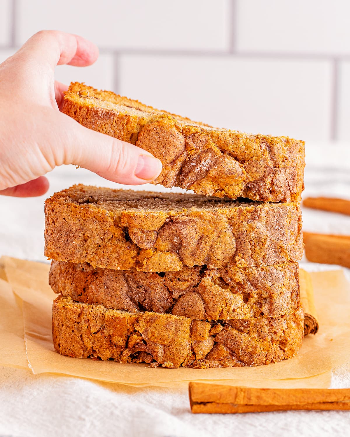 A stack of cinnamon topped bread with a hand lifting the top piece up off the stack. 