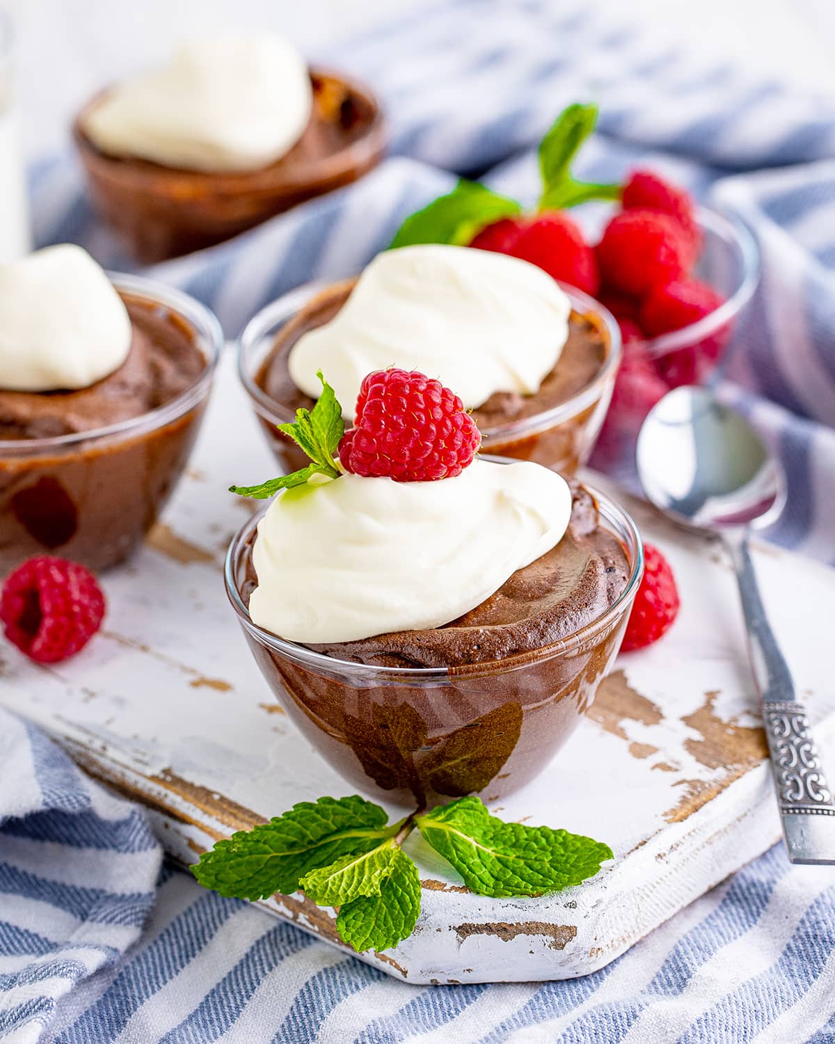 Bowls of fluffy chocolate mousse with whipped cream and raspberries on top.