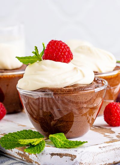 A close up of a bowl of chocolate mousse topped with whipped cream, and a raspberry.