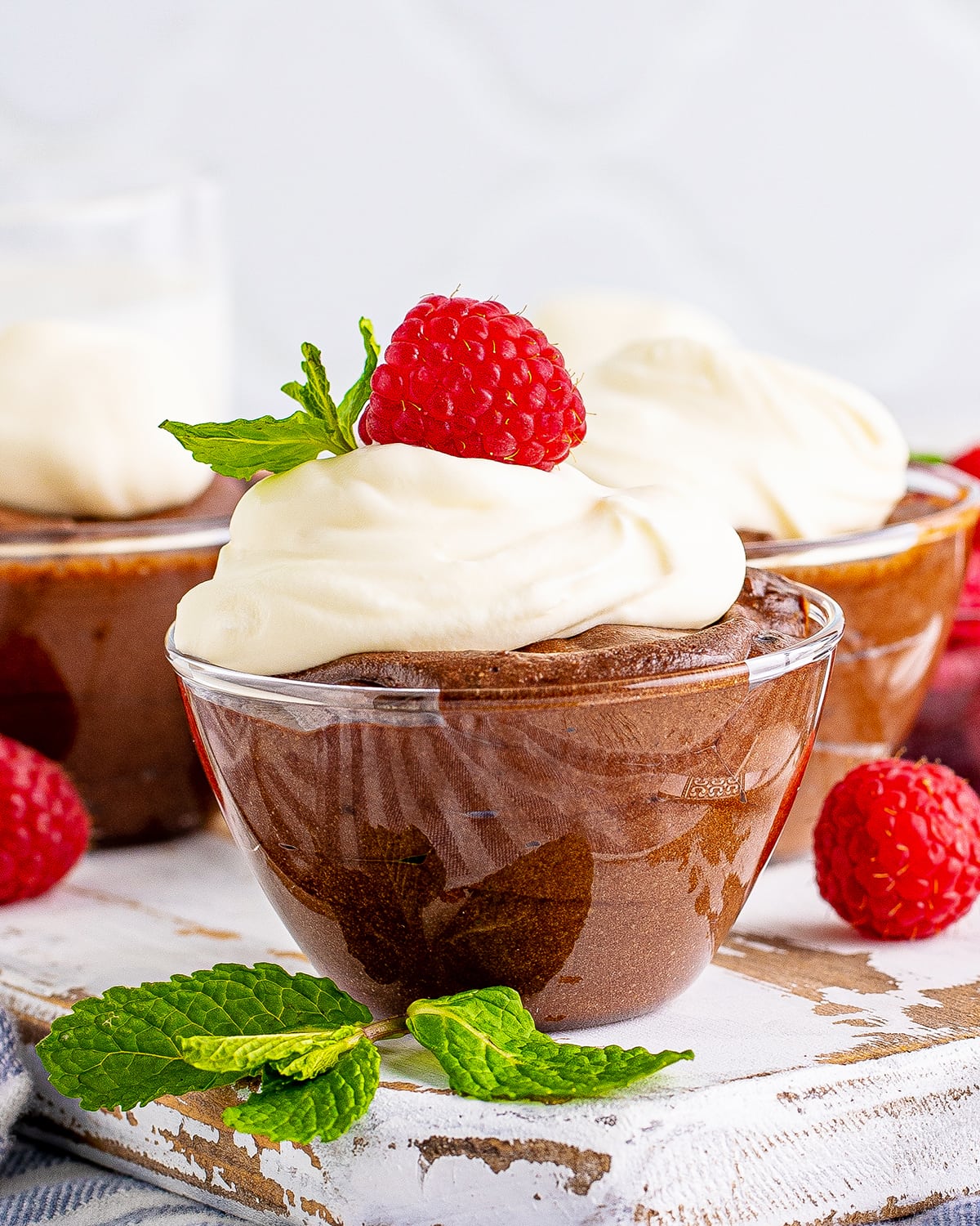 A close up of a bowl of chocolate mousse topped with whipped cream, and a raspberry.
