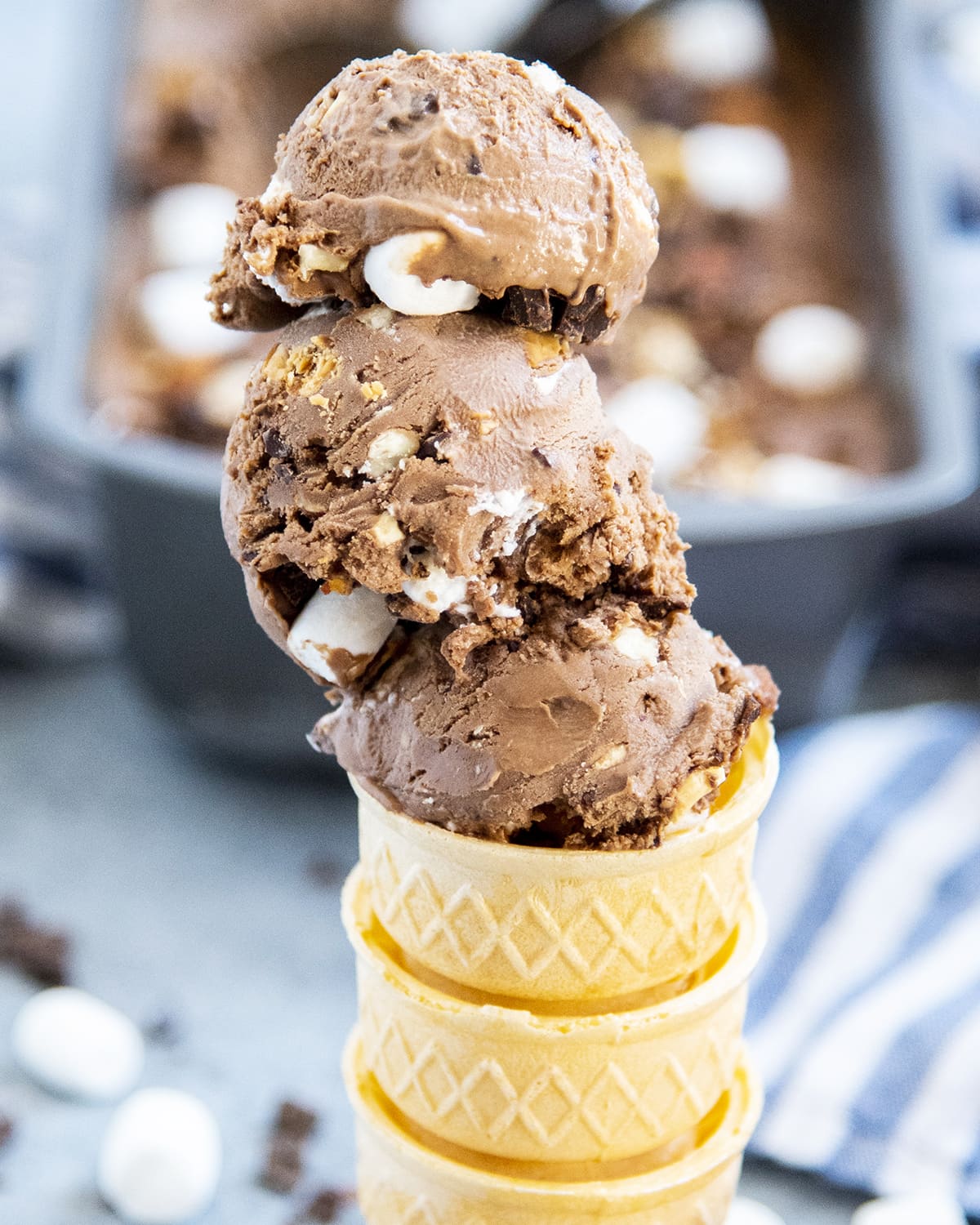 an ice cream cone topped with three scoops of rocky road ice cream.