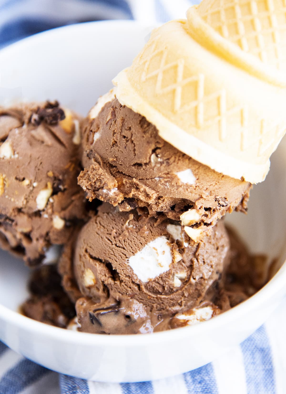 A close up of rocky road ice cream in a bowl topped with an upside down ice cream cone.