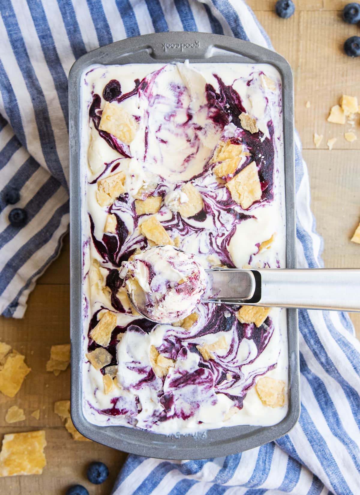 An overhead photo of a container of ice cream swirled with blueberry sauce and a scoop out of it.
