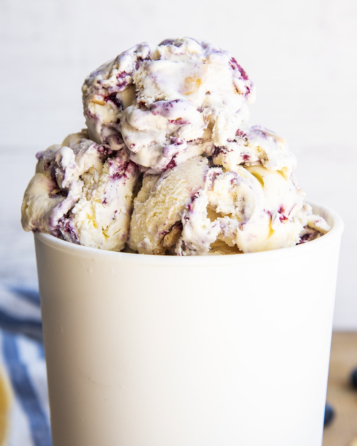 A white ice cream container with three scoops of blueberry swirled ice cream on top.