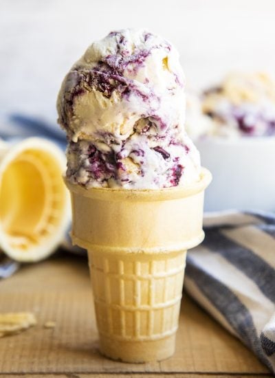 A cone of ice cream with two scoops of vanilla ice cream with blueberry swirls.