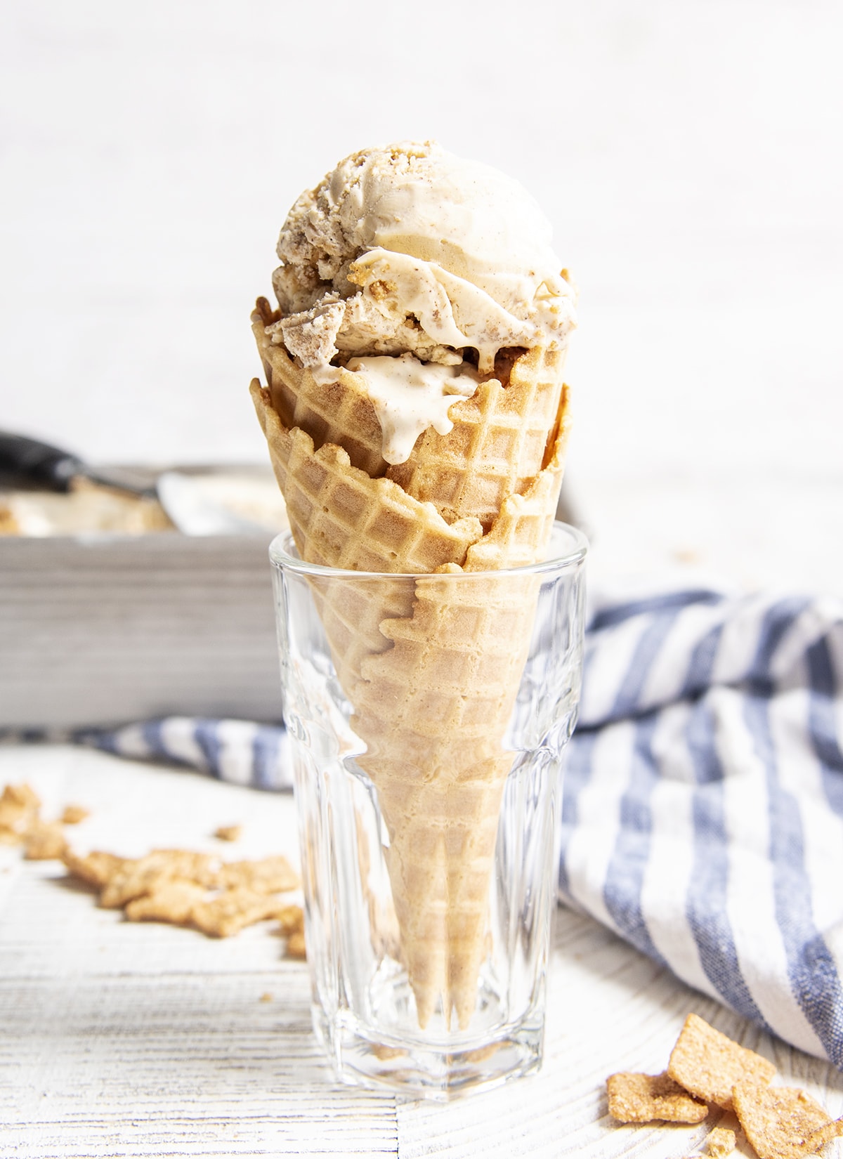 A scoop of cinnamon Toast Crunch Ice Cream in a cone, standing in a glass.