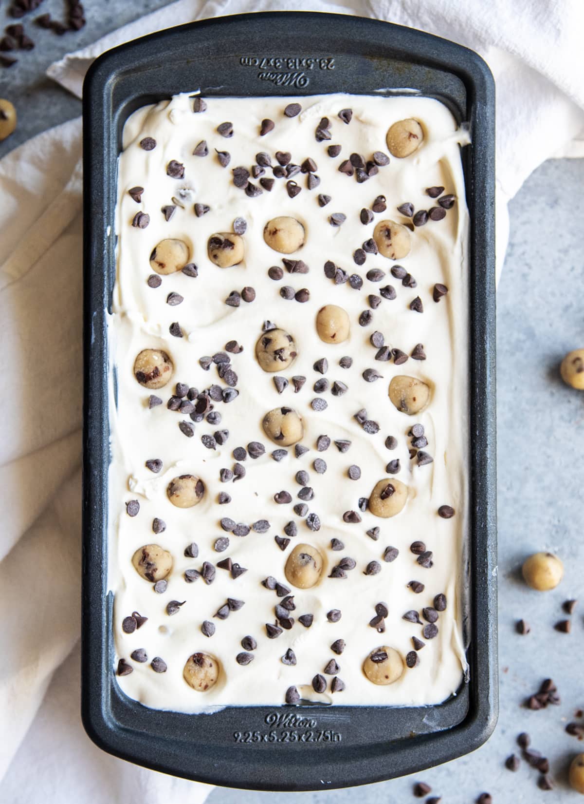 An overhead photo of a container of vanilla ice cream topped with chocolate chips and balls of cookie dough.