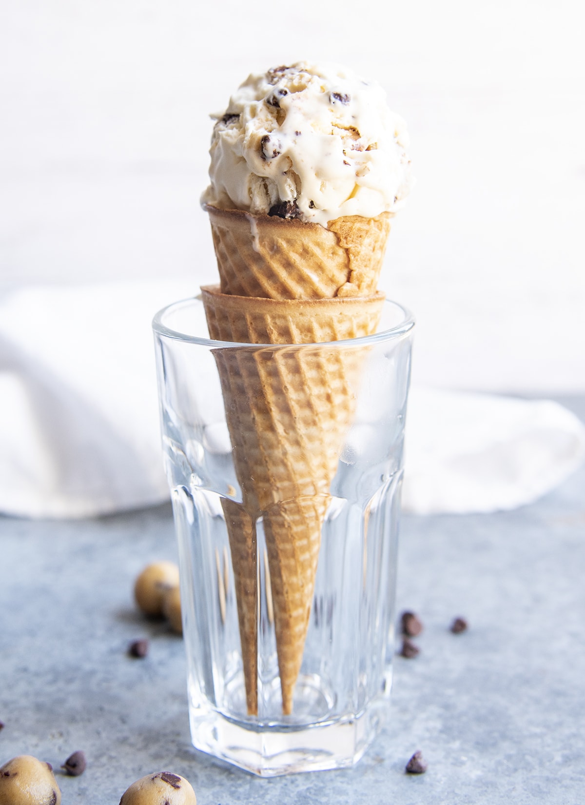 A scoop of cookie dough ice cream on top of two ice cream cones in a glass cup.