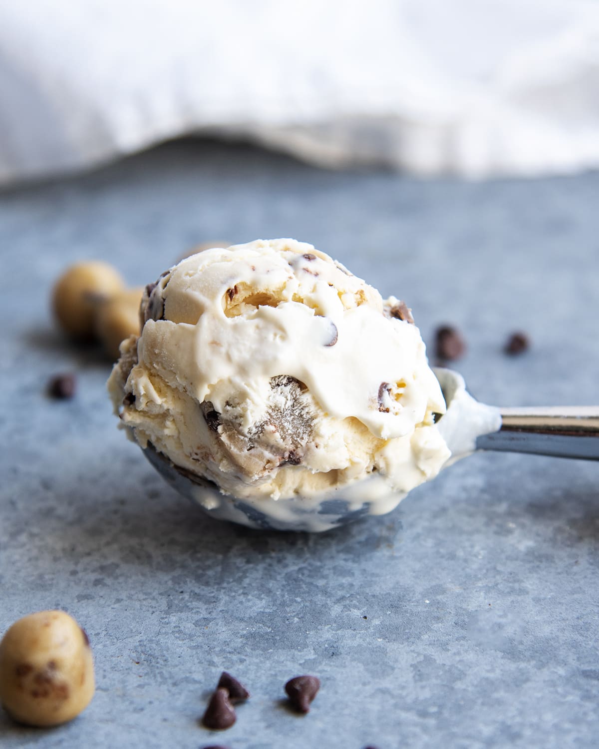 A scoop of chocolate chips cookie dough ice cream on a gray surface.