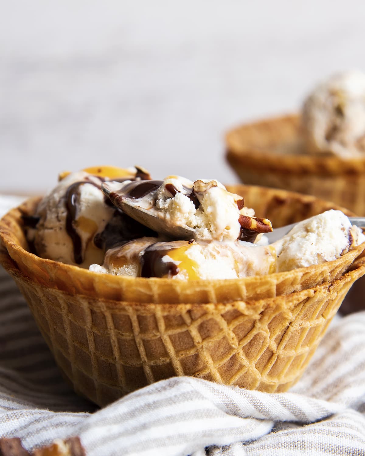 A bowl of ice cream in a waffle cone bowl topped with hot fudge and caramel syrup. 