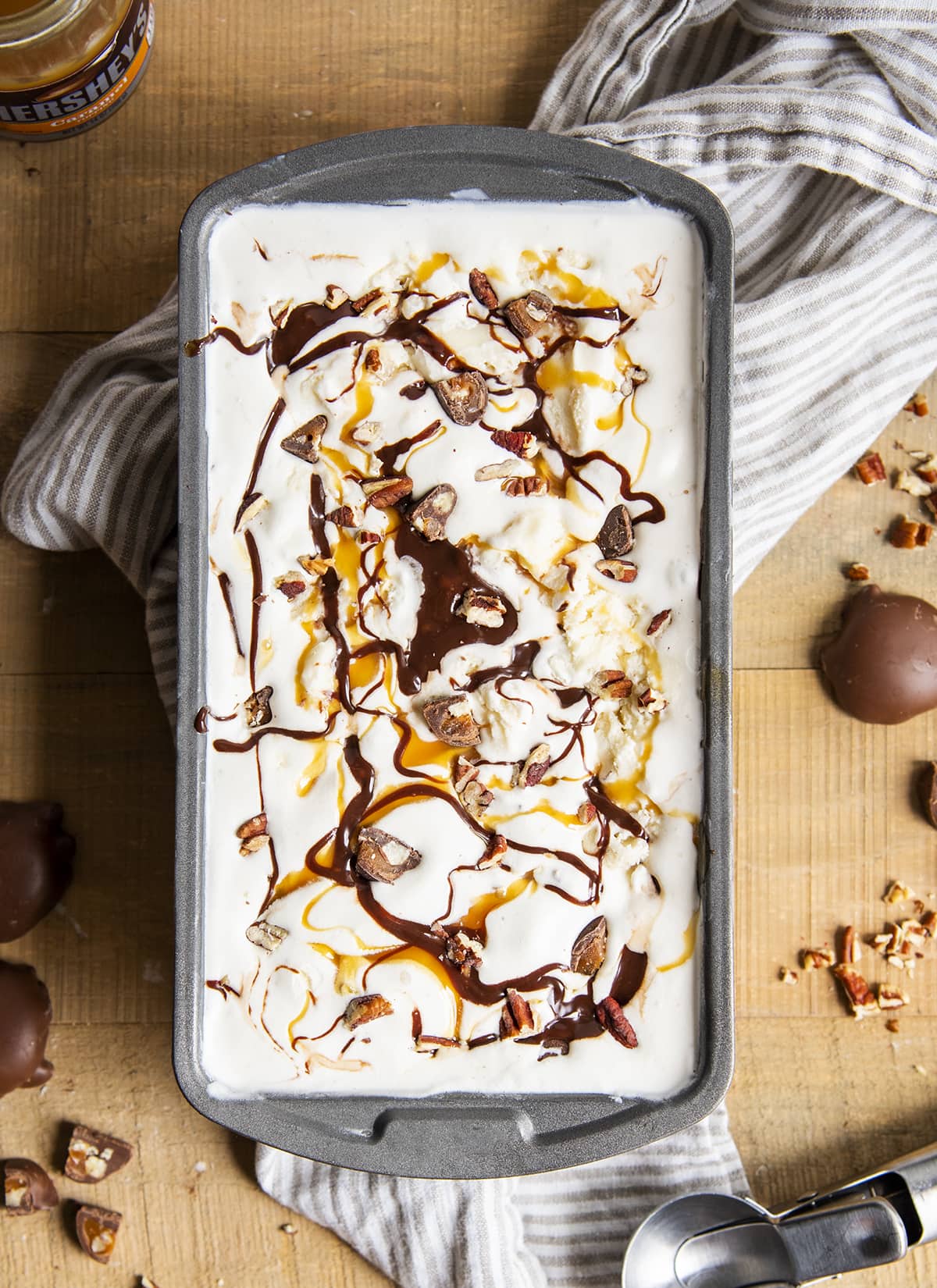A metal container full of vanilla ice cream swirled with chocolate and caramel syrups.