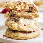 A stack of large white chocolate raspberry cookies with the top cookie cut in half showing the middle of the cookie.