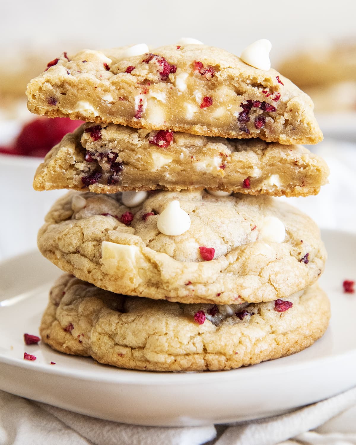 A stack of large white chocolate raspberry cookies with the top cookie cut in half showing the middle of the cookie.
