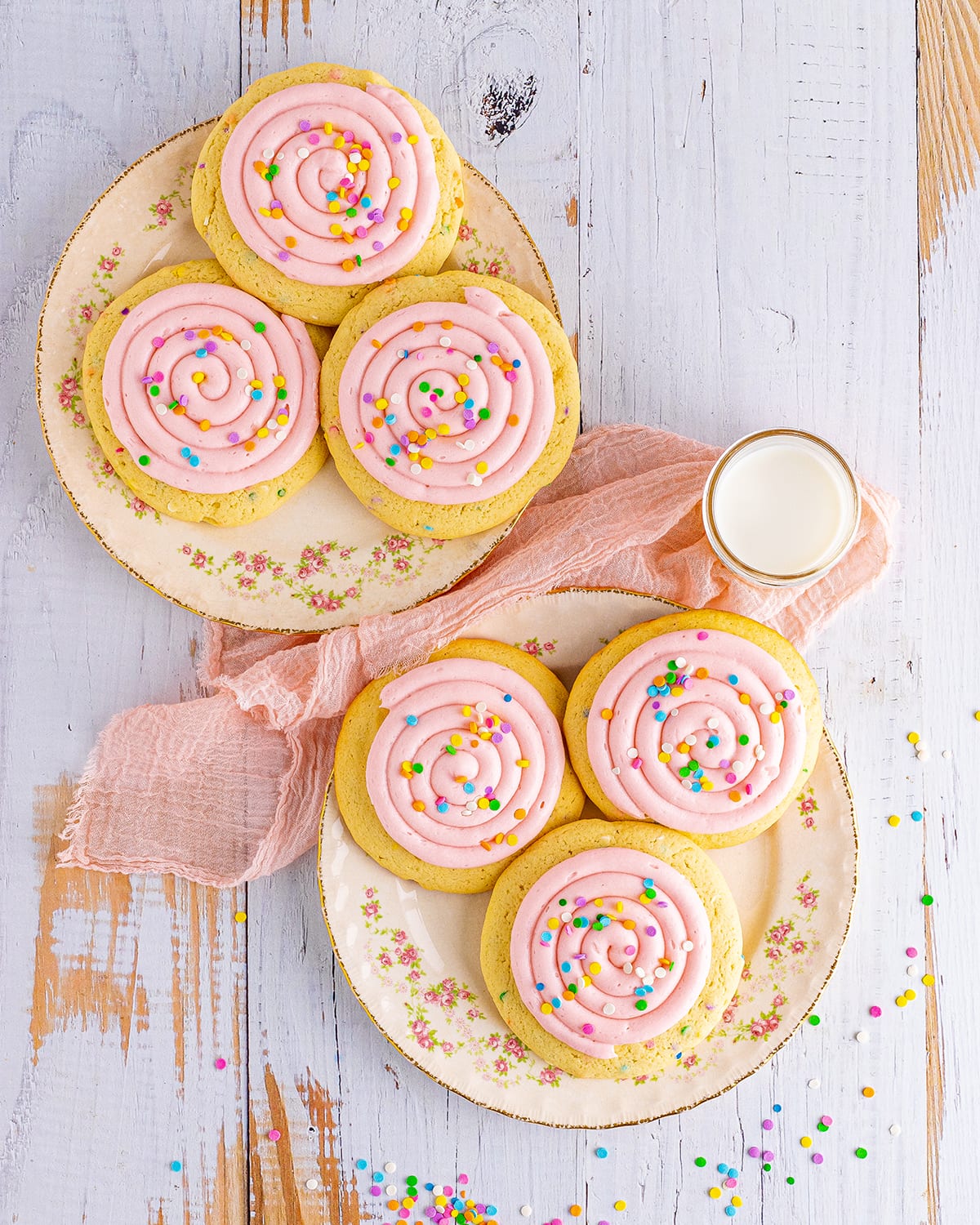 An overhead photo of two plates of pink frosted cookies with confetti sprinkles on top.