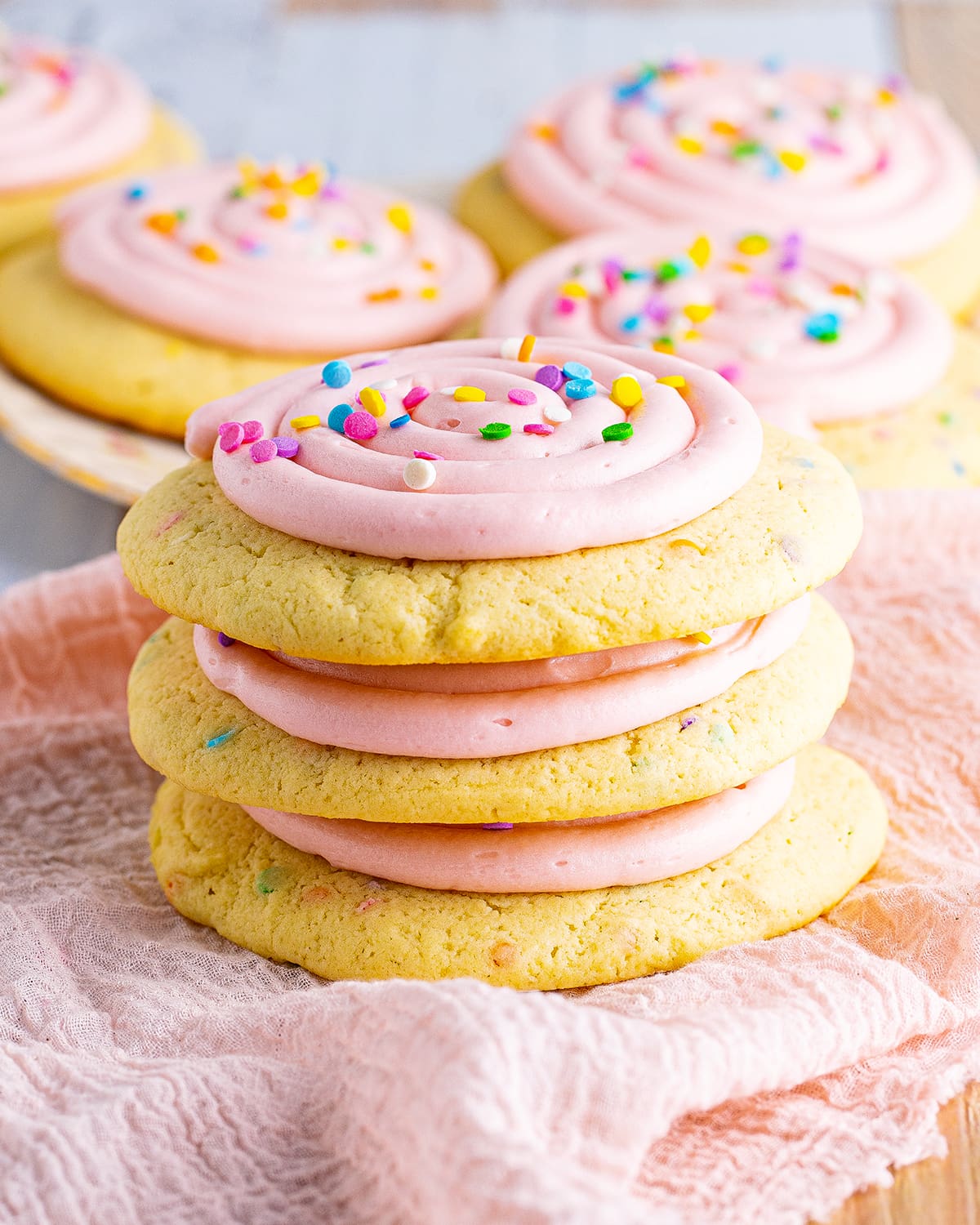 A stack of three confetti cake cookies with pink frosting and sprinkles on top of them.